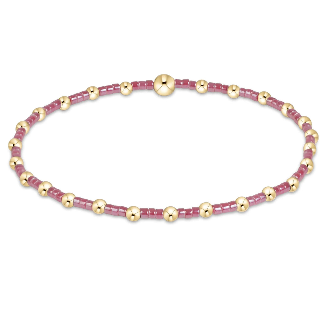 A delicate beaded bracelet featuring alternating translucent dusty pink beads and polished gold spacer beads, completed with a large round gold bead clasp at the top center, shown on a plain white background.