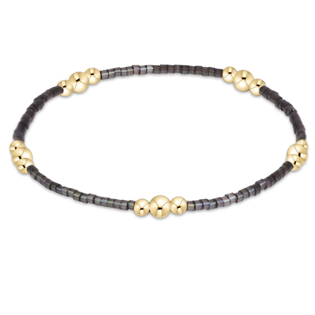 A beaded stretch bracelet featuring dark gray faceted disc beads and polished gold ball accents, displayed on a clean white background.