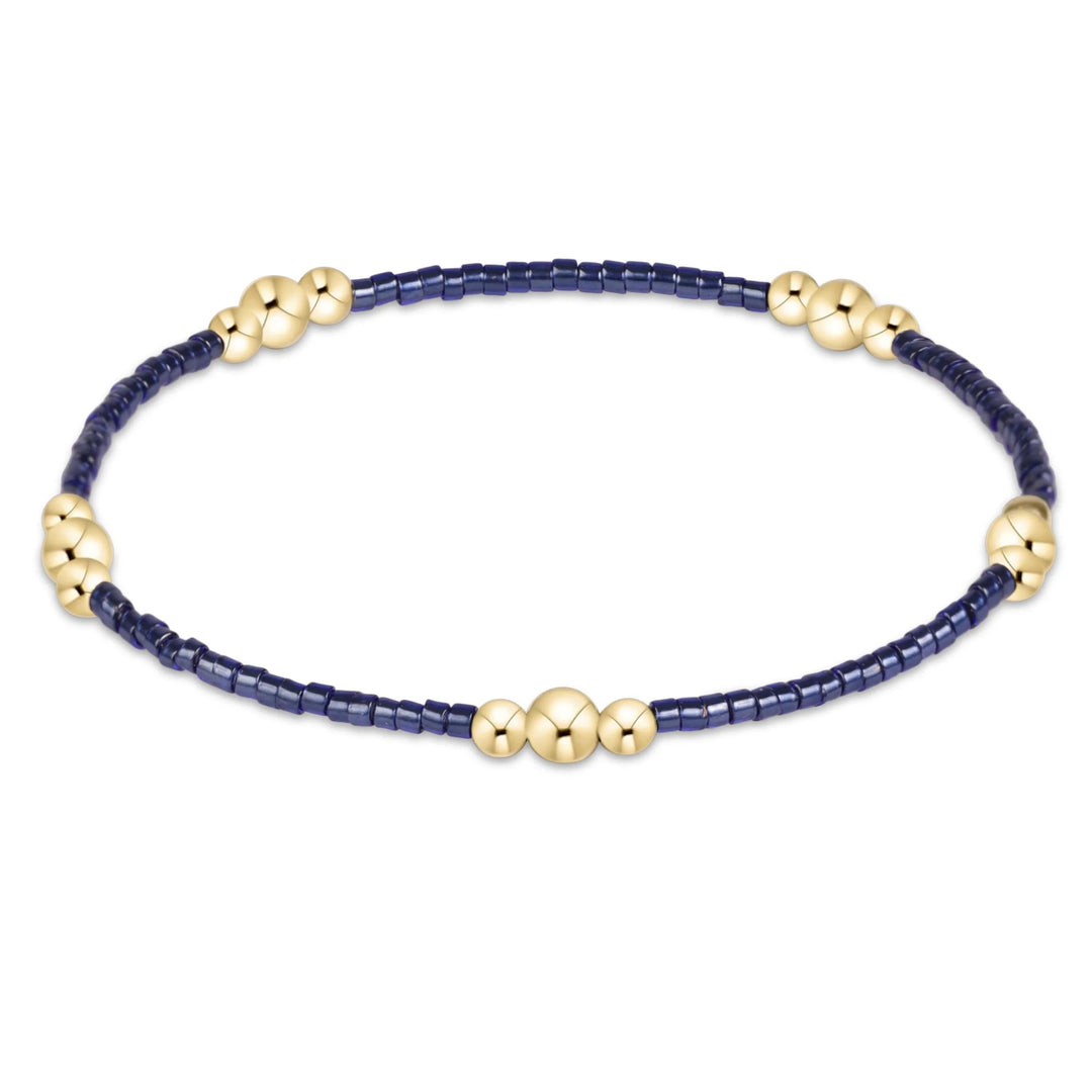 A beaded stretch bracelet featuring dark navy blue cylindrical beads and shiny gold metallic accents, including three larger gold beads on the front and smaller gold floral clusters along the sides, displayed on a clean white background.