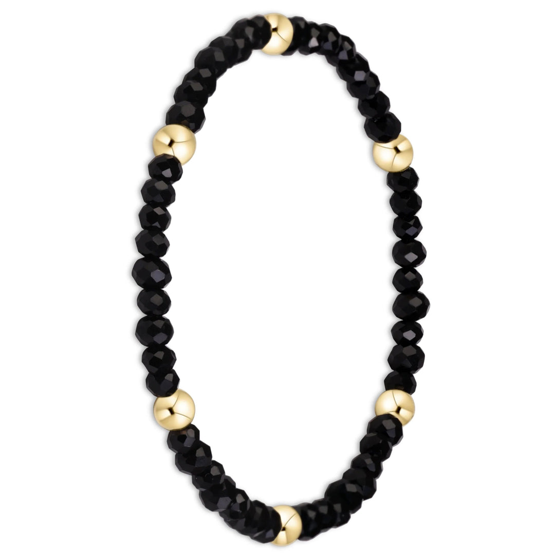 A beaded stretch bracelet featuring faceted black beads and polished gold spacer beads, displayed on a clean white background.