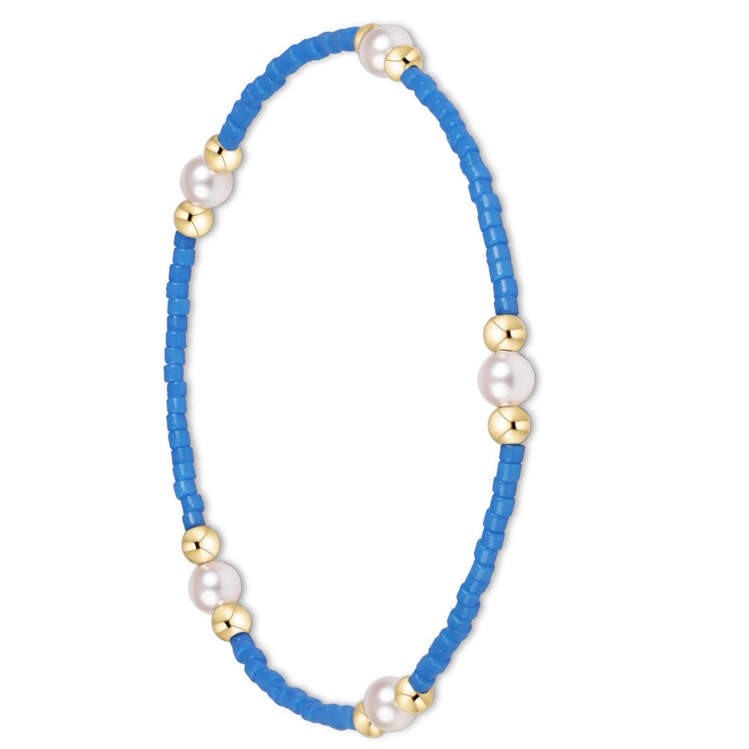 A delicate blue beaded bracelet with alternating white pearl beads and small gold spacer beads, displayed on a clean white background.