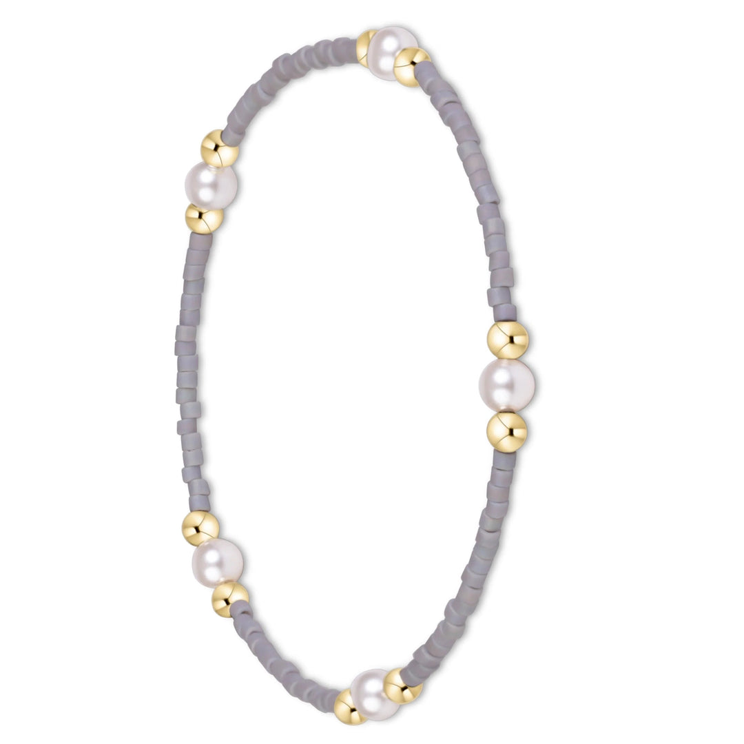 A delicate beaded bracelet with light gray cylindrical beads, accented by three large white pearls and several polished gold spacer beads, shown on a plain white background.