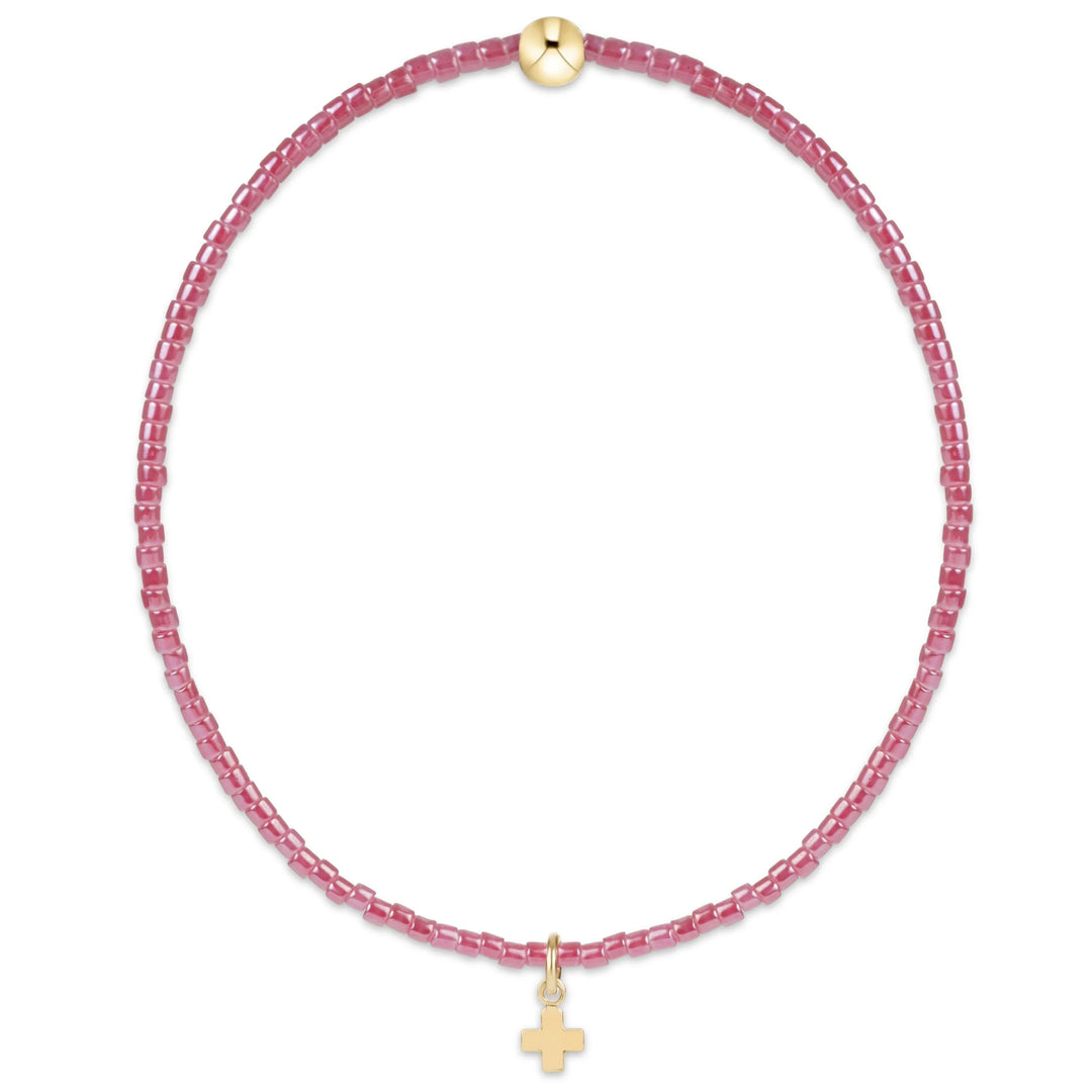 A delicate pink beaded necklace with a small gold cross pendant and a gold clasp, displayed on a clean white background.
