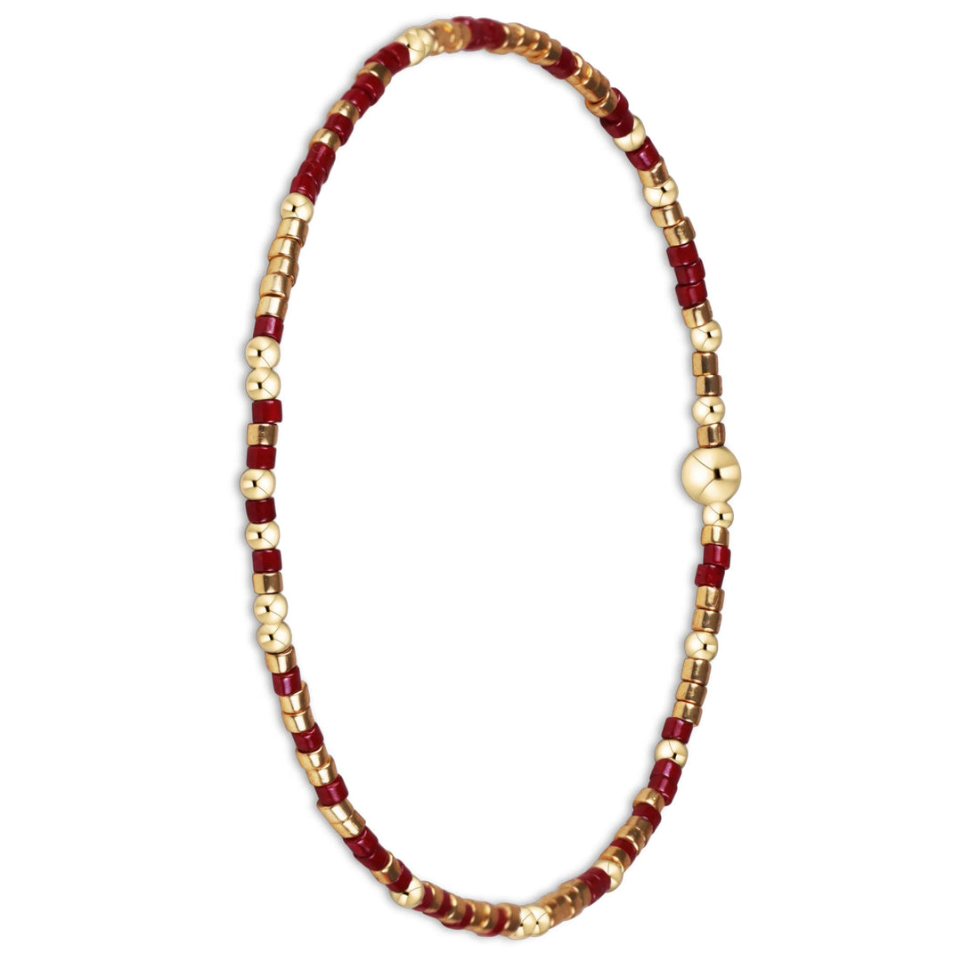 A delicate beaded bracelet with alternating red cylindrical beads and metallic gold spacer beads, featuring a polished gold clasp, shown on a plain white background.