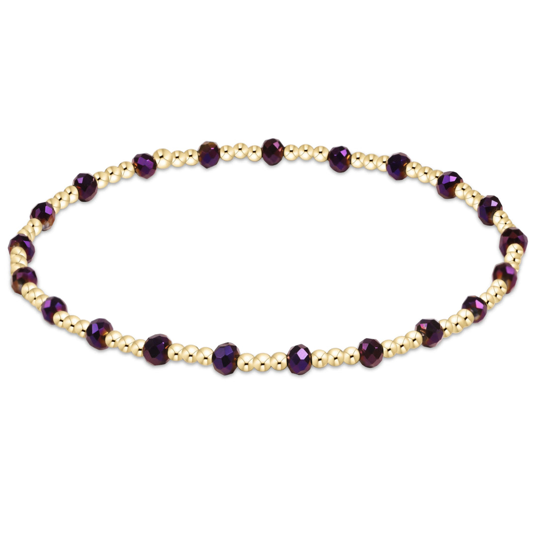A beaded stretch bracelet featuring faceted dark purple beads and small metallic gold beads, arranged in an oval shape on a plain white background.