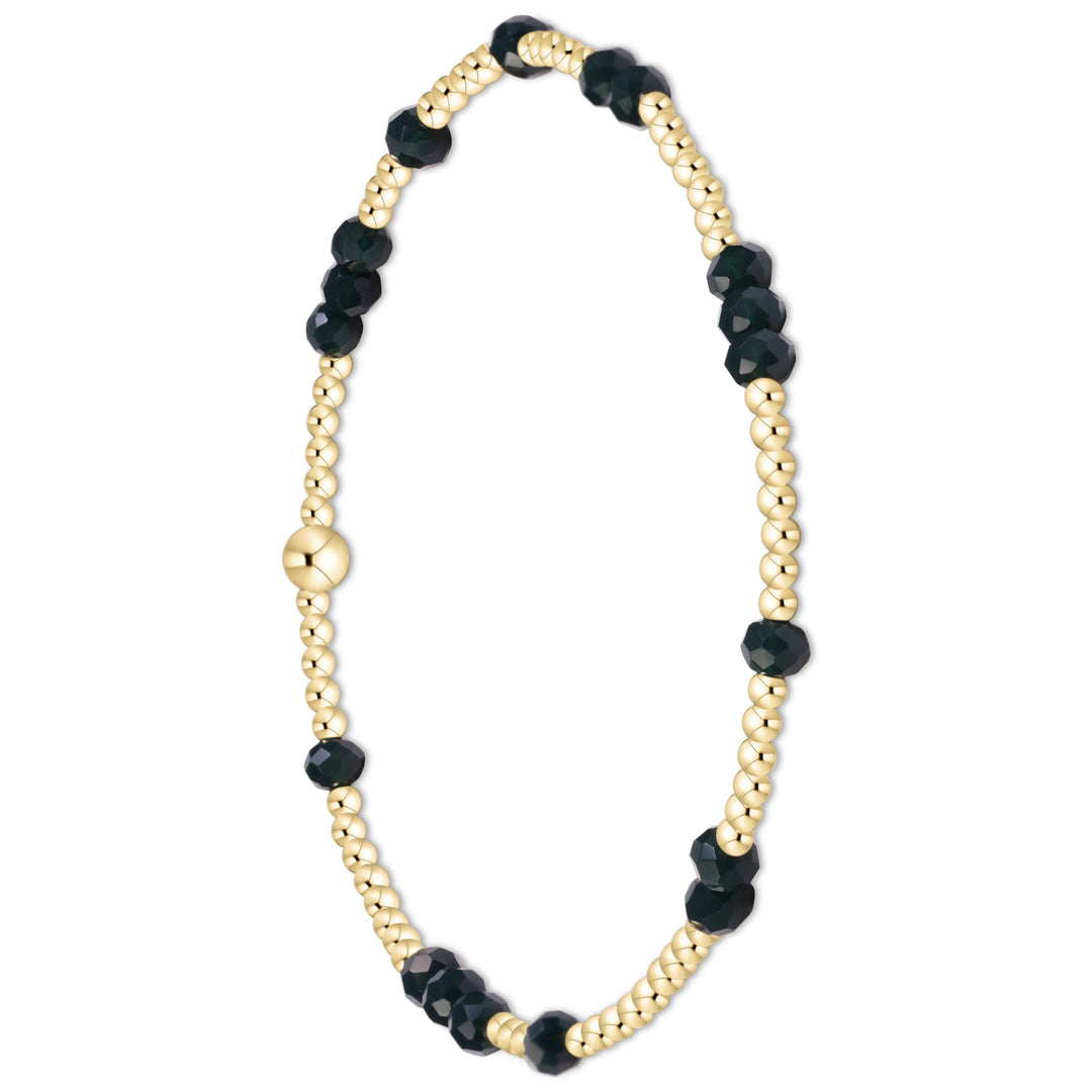 A beaded bracelet featuring alternating strands of polished gold-toned round beads and faceted dark green beads, with a central gold-toned spacer bead, shown on a plain white background.