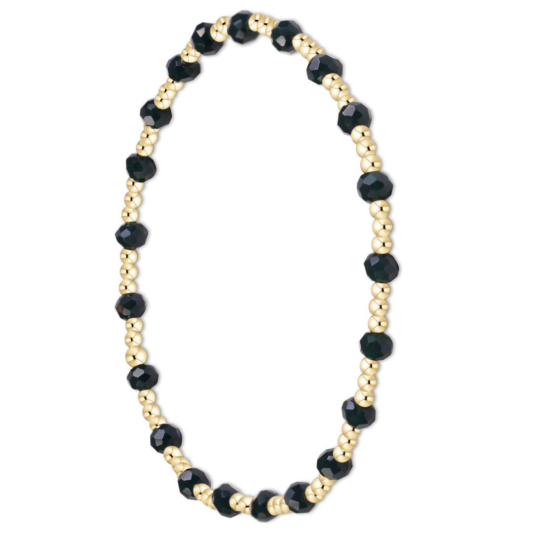 A beaded stretch bracelet featuring faceted black beads alternating with small metallic gold beads, displayed on a clean white background.