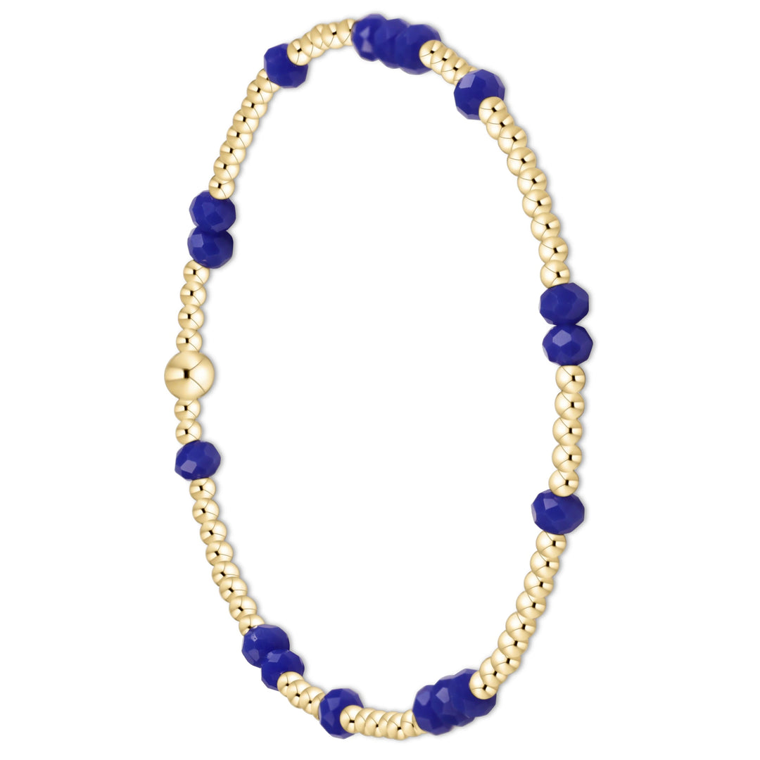 A beaded bracelet featuring small gold-toned round beads interspersed with larger faceted deep blue beads, completed with a gold-toned clasp, shown on a plain white background.