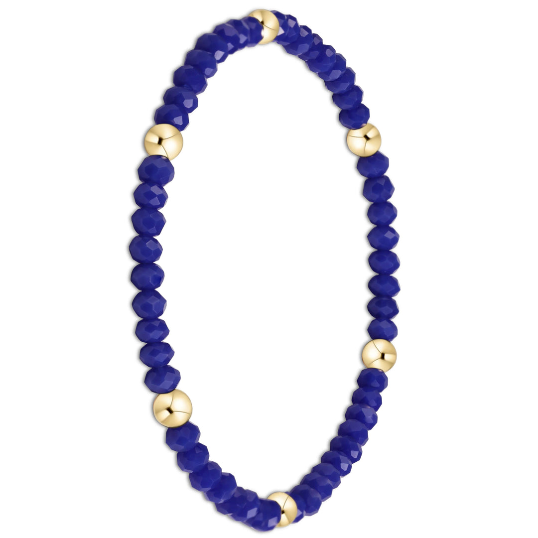 A beaded stretch bracelet featuring faceted deep blue beads and polished gold spacer beads, displayed on a clean white background.