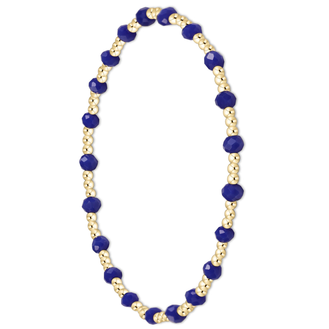 A beaded stretch bracelet featuring faceted deep blue beads and small metallic gold beads, arranged in an oval shape on a plain white background.