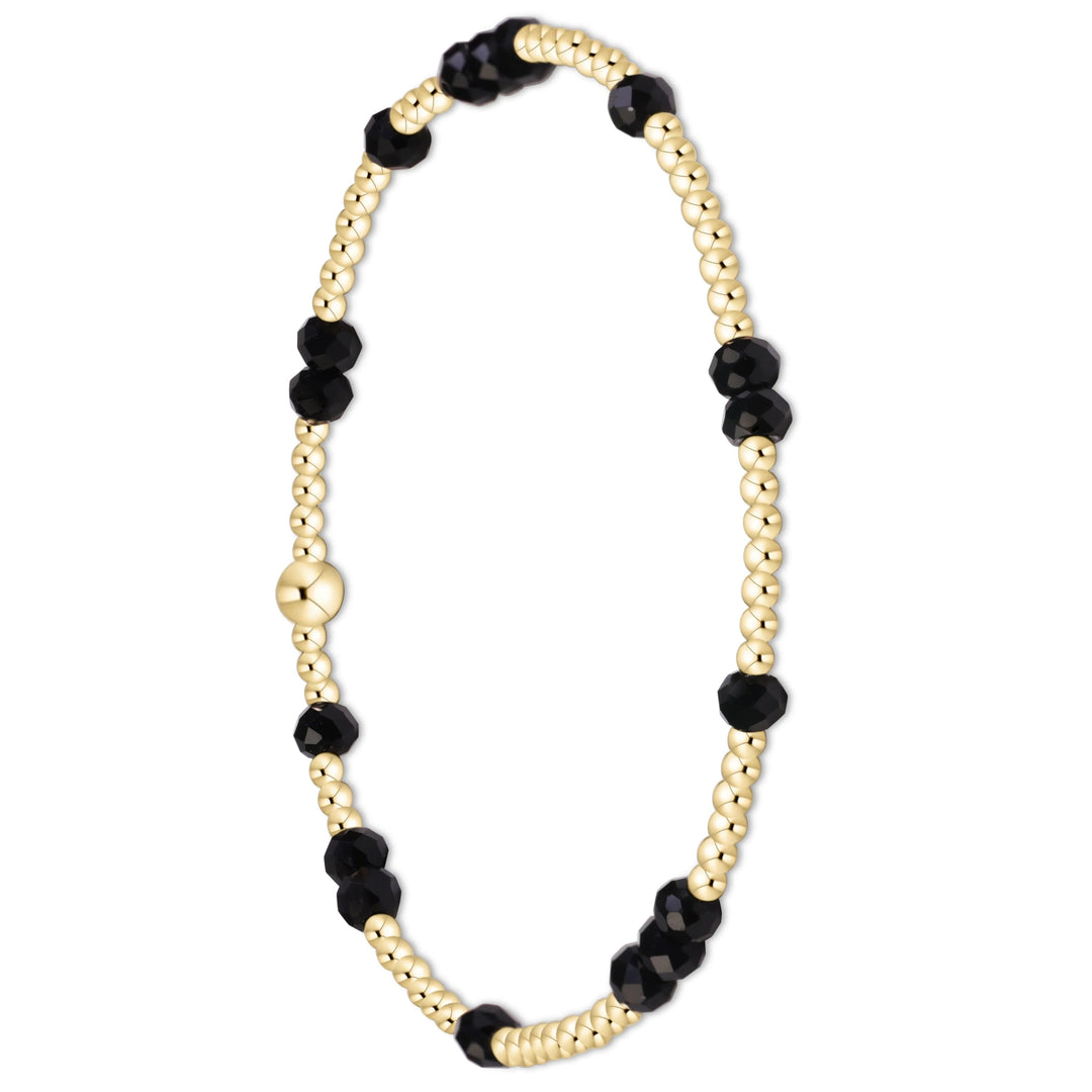 A beaded stretch bracelet featuring alternating strands of small gold-toned beads and faceted black beads, with a polished gold-toned clasp, shown on a solid white background.