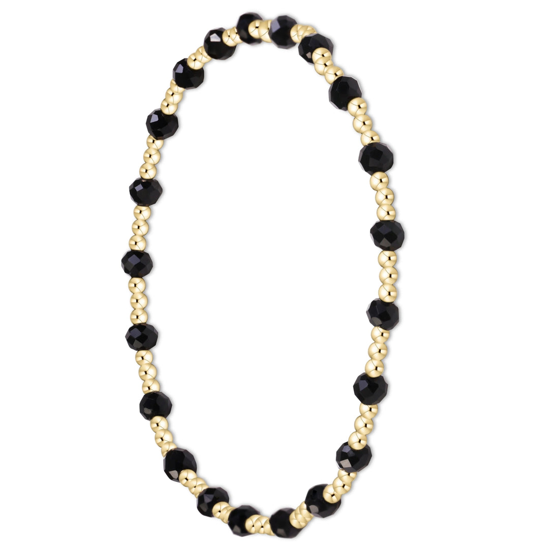 A beaded stretch bracelet featuring alternating faceted black beads and small metallic gold beads, displayed on a clean white background.