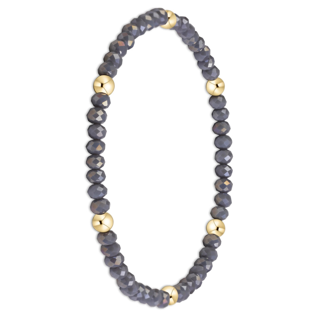 A beaded stretch bracelet featuring faceted dark gray beads and alternating polished gold-toned round spacers, displayed on a clean white background.
