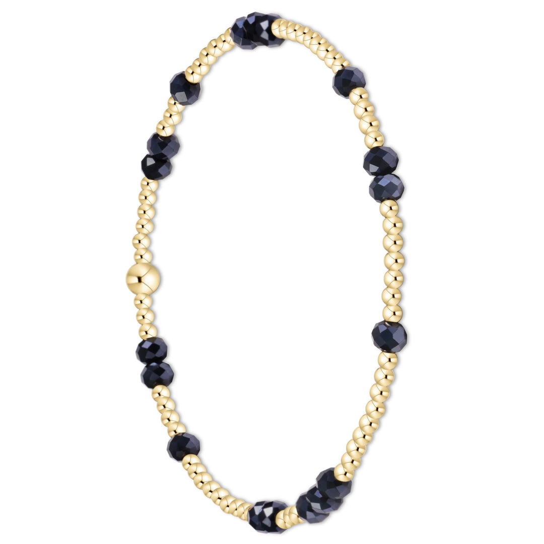 A delicate beaded bracelet featuring alternating strands of polished gold-tone beads and faceted dark navy blue beads, with a central gold-tone bead and clasp, shown on a plain white background.