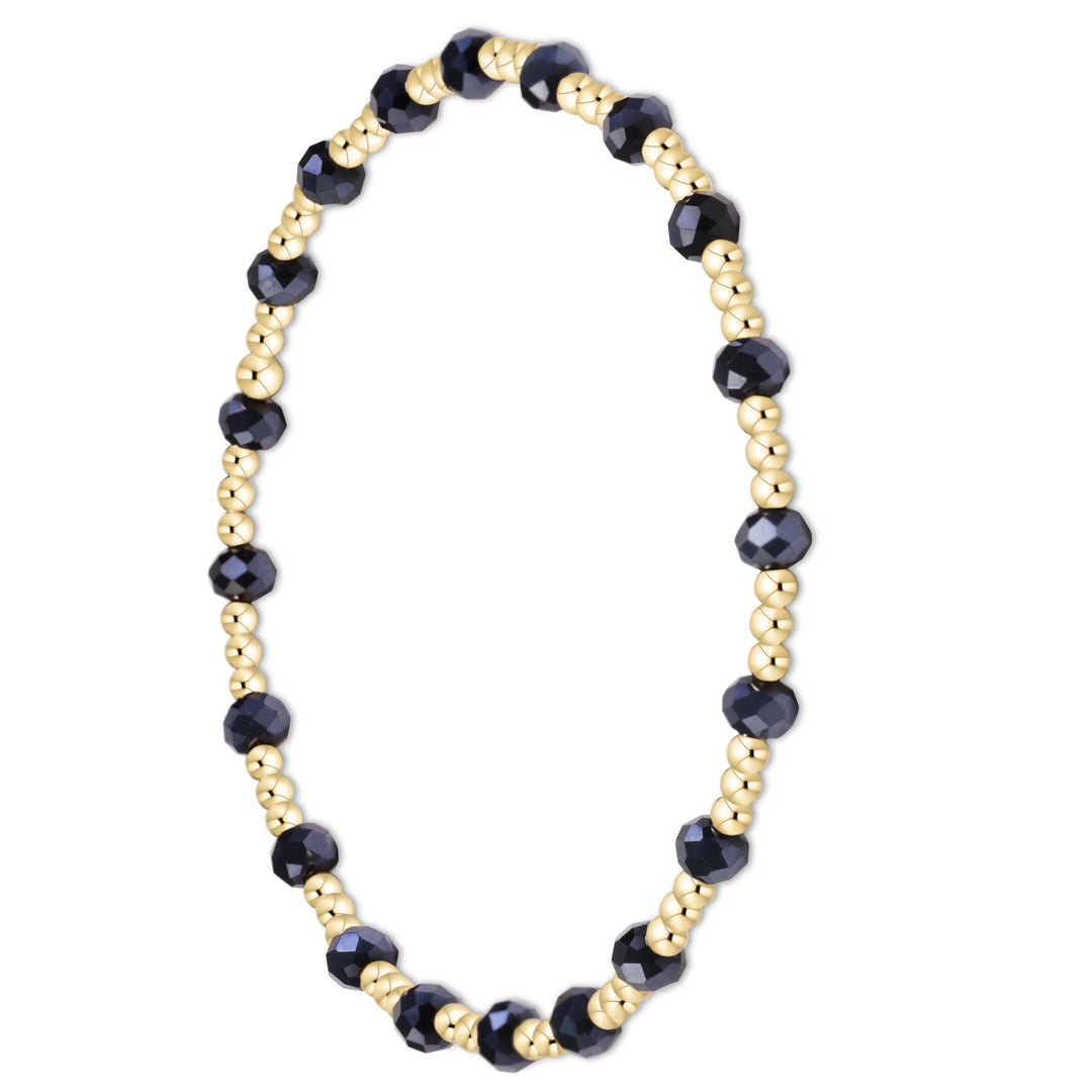 A beaded stretch bracelet featuring faceted dark navy blue beads alternating with small metallic gold spacer beads, shown on a clean white background.