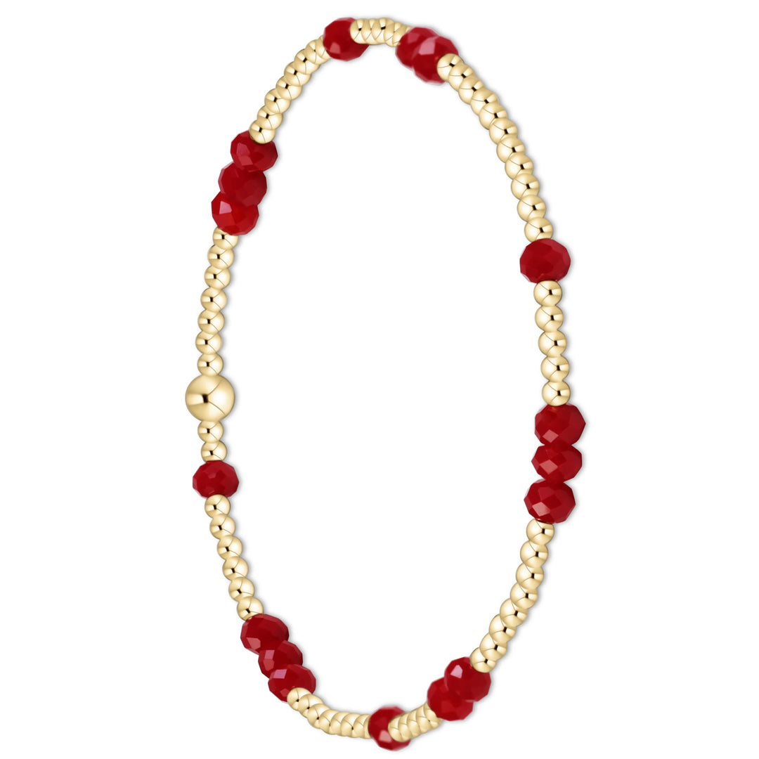 A beaded stretch bracelet featuring faceted red beads alternating with small gold-toned metallic beads, shown on a plain white background.