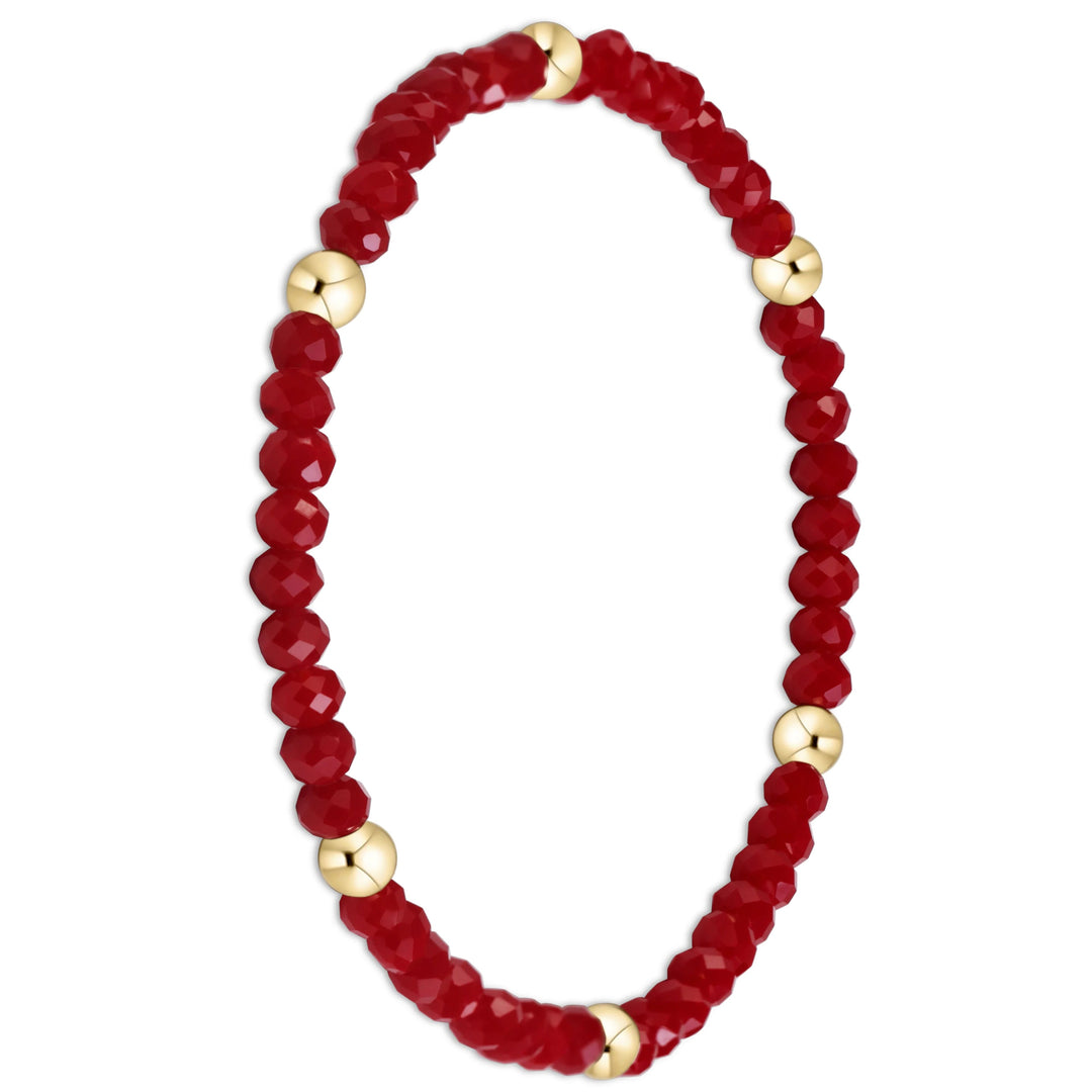 A beaded stretch bracelet featuring faceted deep red beads and polished gold spacer beads, displayed on a clean white background.
