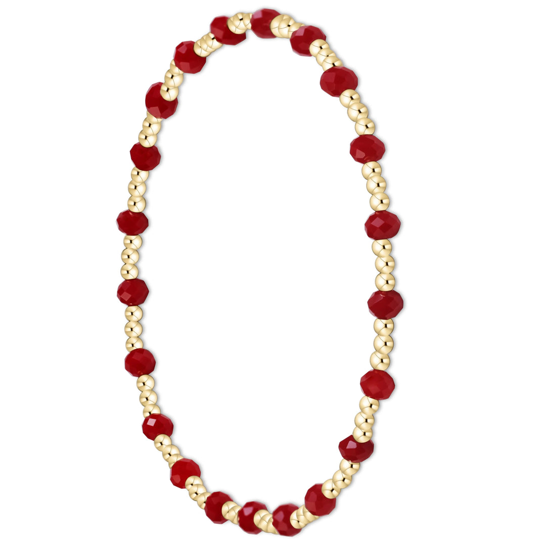 A beaded stretch bracelet featuring faceted deep red beads and small metallic gold beads, arranged in an oval shape on a solid white background.