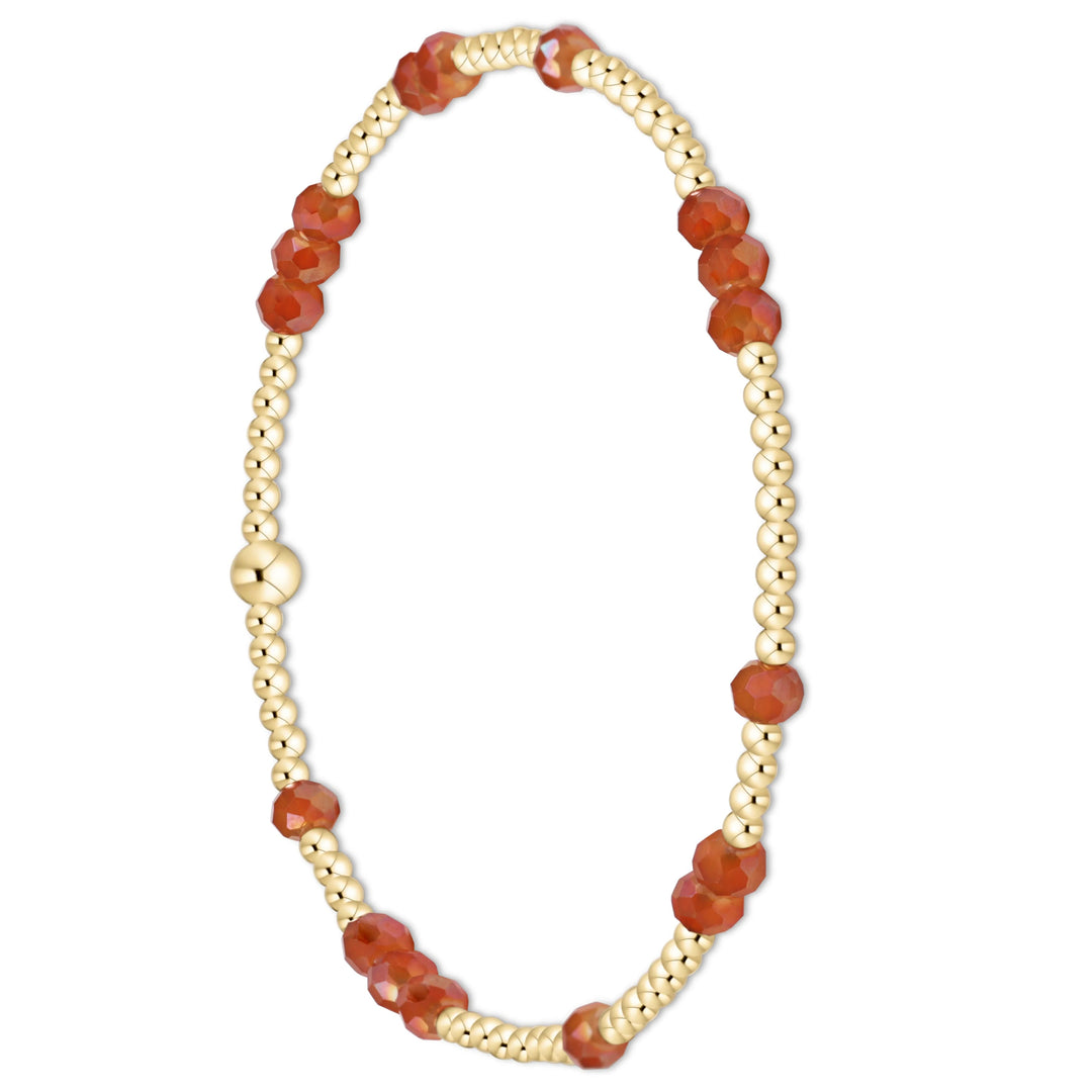 A delicate beaded bracelet featuring faceted orange-red gemstone beads alternating with small metallic gold beads, displayed on a clean white background.