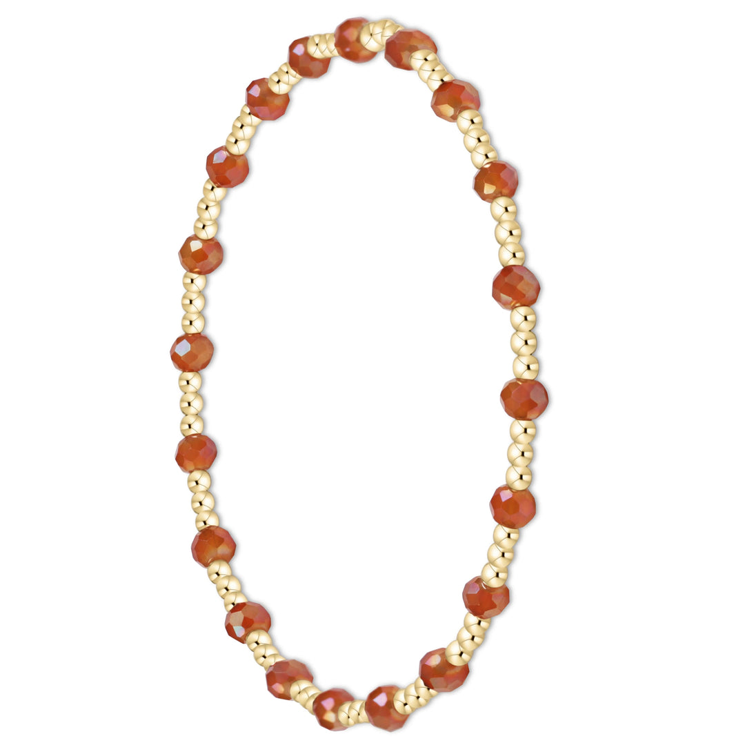 A beaded stretch bracelet featuring faceted orange-red gemstone beads and small metallic gold spacer beads, displayed on a clean white background.