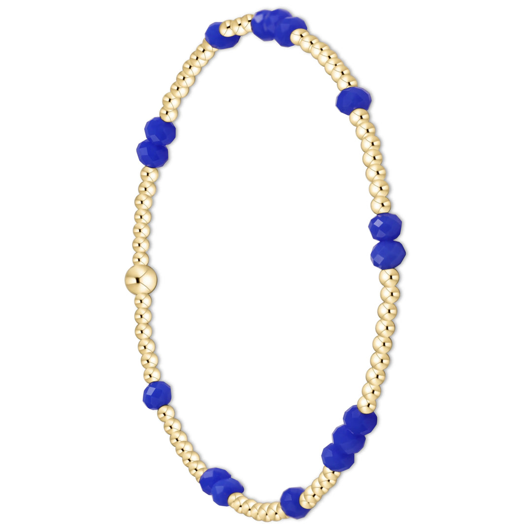A delicate beaded bracelet featuring alternating strands of small gold-toned beads and larger faceted royal blue beads, with a matching gold-toned bead clasp, shown on a solid white background.