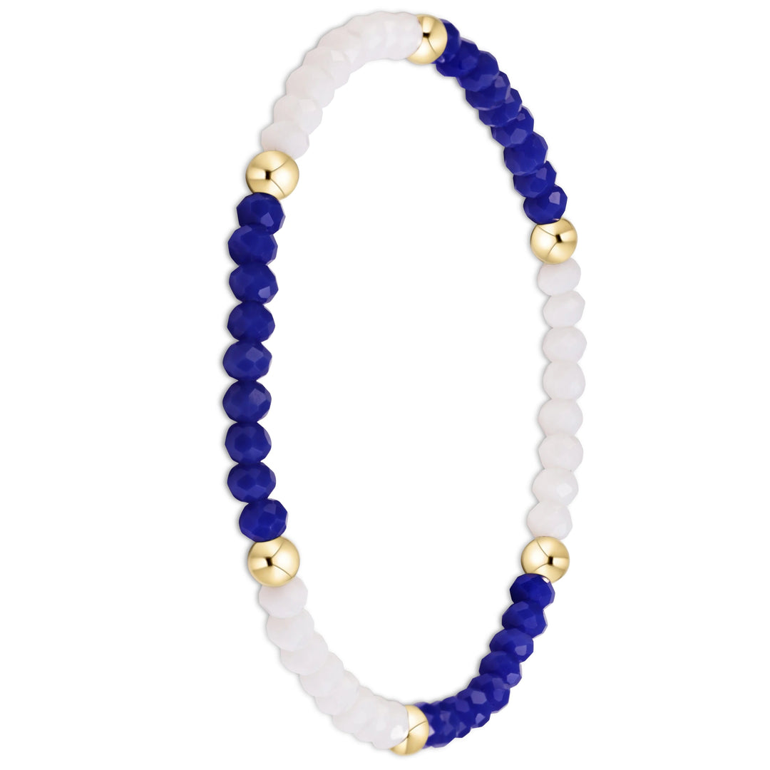 A beaded stretch bracelet featuring faceted deep blue beads, matte white beads, and polished gold spacer beads, arranged in an oval shape on a plain white background.