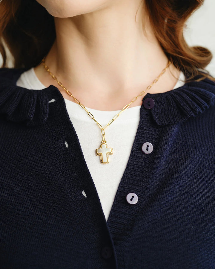 Person wearing a gold necklace with a cross pendant, dressed in a navy cardigan and white shirt.
