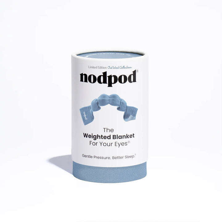 A cylindrical white product box for nodpod The Weighted Blanket For Your Eyes, featuring a light blue illustration of the weighted blanket and a solid light blue base, set against a clean white background.
