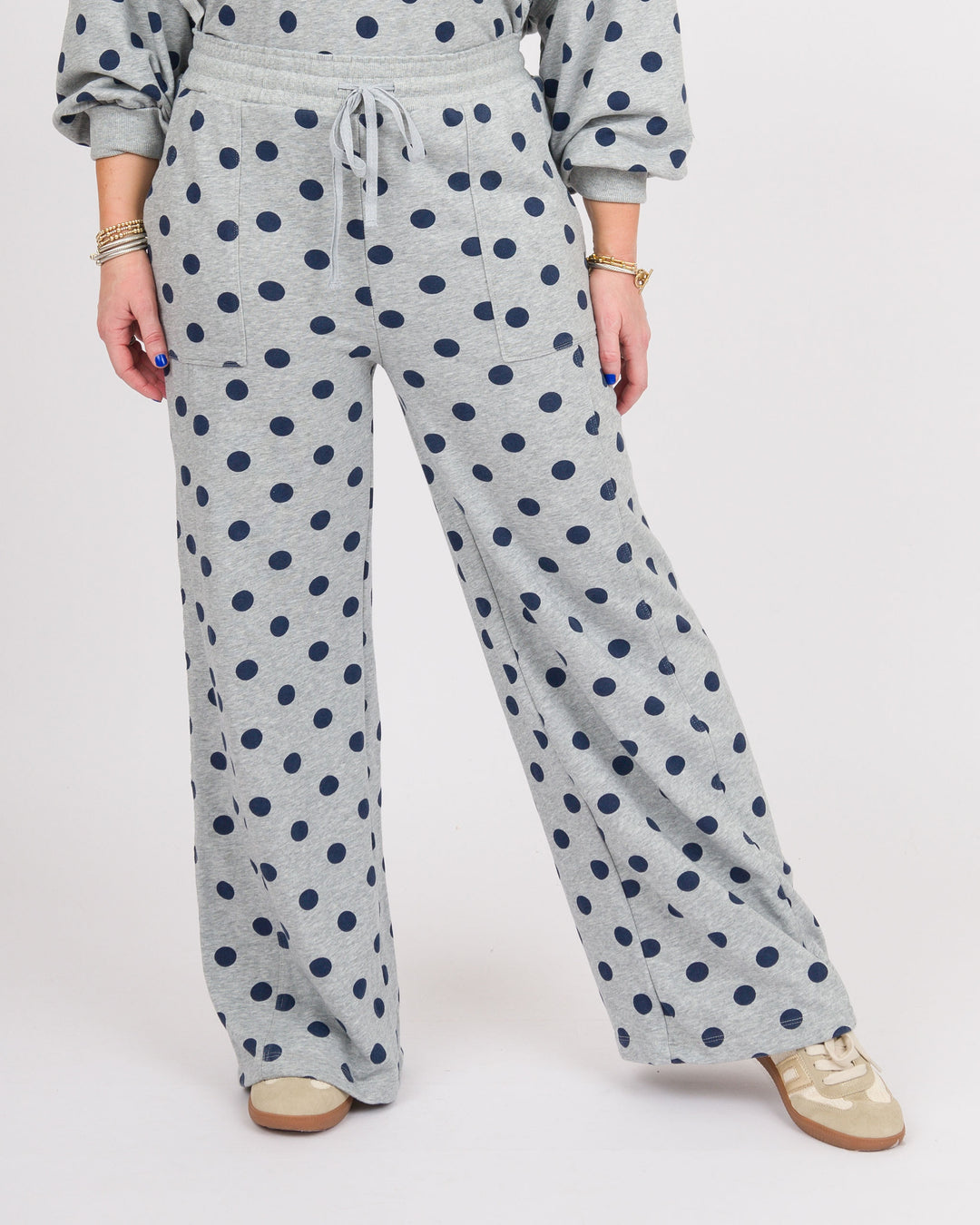 A person wearing light heather gray wide-leg sweatpants with a navy blue polka dot pattern, paired with a matching gray sweatshirt and beige sneakers, shown from the waist down on a white studio background.