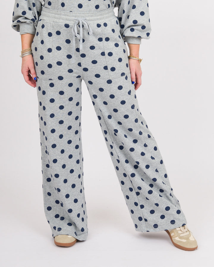 A person wearing light heather gray wide-leg sweatpants with a navy blue polka dot pattern, paired with a matching gray sweatshirt and beige sneakers, shown from the waist down on a white studio background.