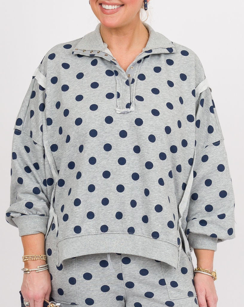A woman modeling a matching two-piece lounge set featuring a light gray sweatshirt and wide-leg pants with dark navy blue polka dots, set against a plain white studio background.