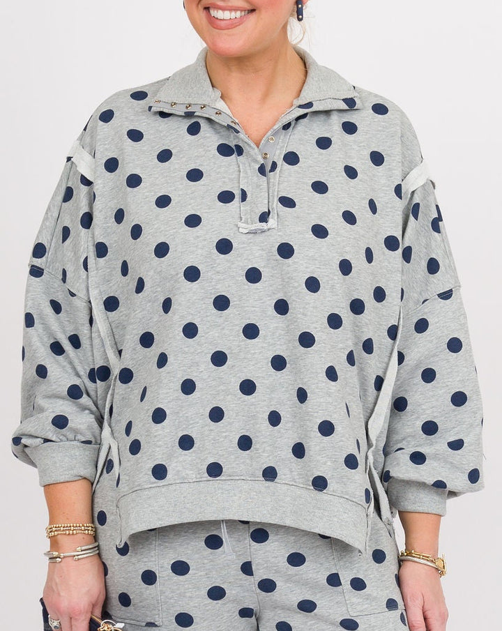 A woman modeling a matching two-piece lounge set featuring a light gray sweatshirt and wide-leg pants with dark navy blue polka dots, set against a plain white studio background.