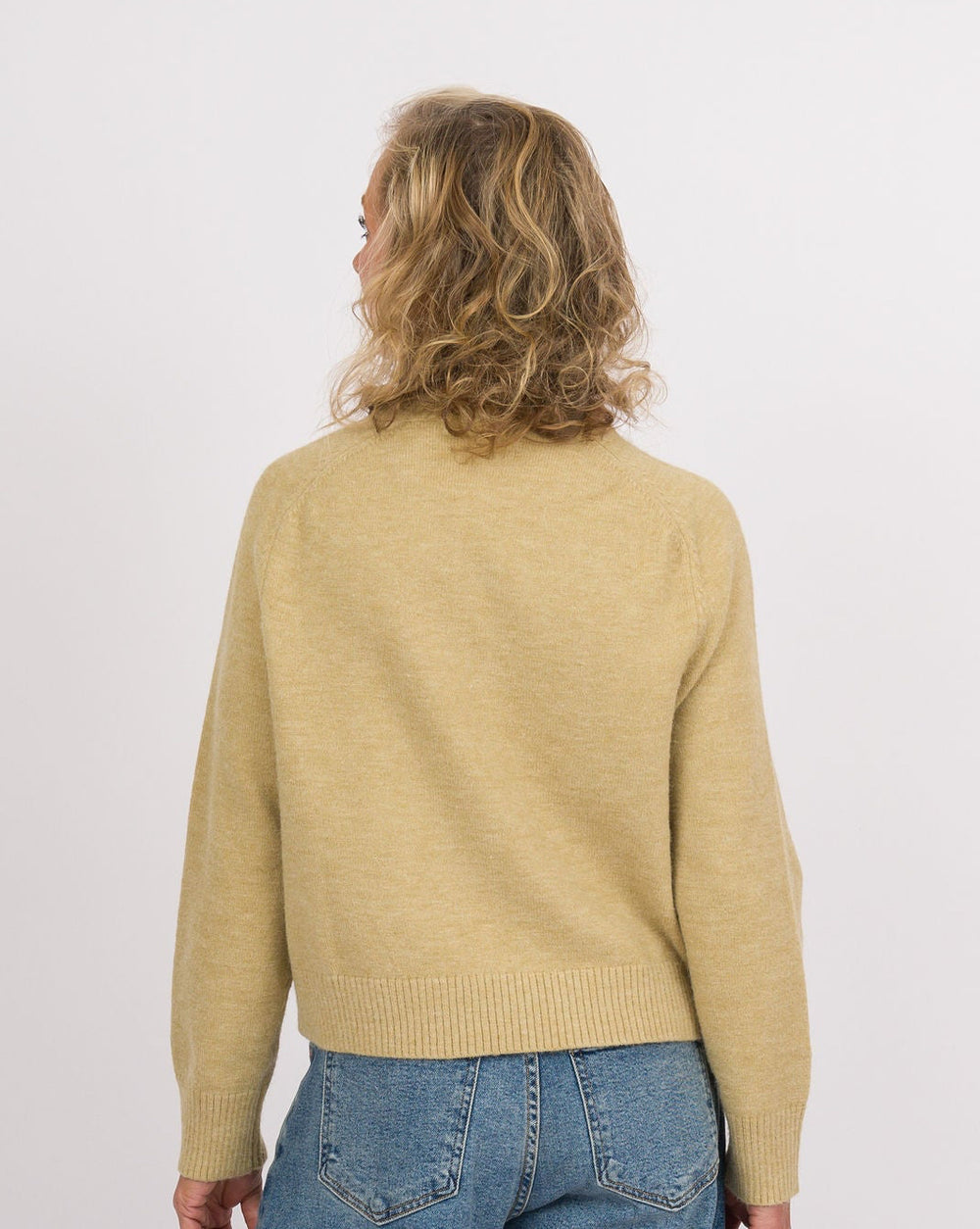 A model shown from the back wearing a light yellow knit sweater, wide-leg blue denim jeans, and black slip-on shoes with beige soles, set against a plain white studio background.