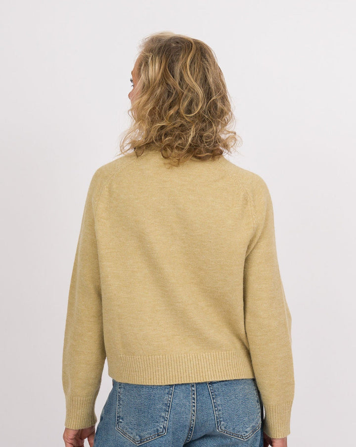 A model shown from the back wearing a light yellow knit sweater, wide-leg blue denim jeans, and black slip-on shoes with beige soles, set against a plain white studio background.