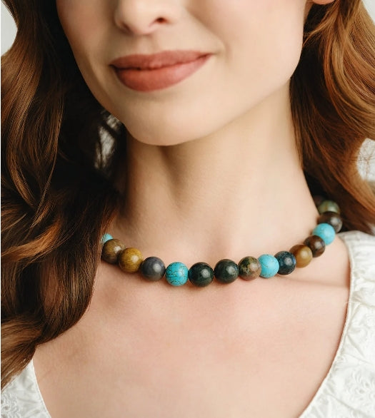 A close-up of a woman wearing a beaded necklace made of round natural stone beads in turquoise, dark green, brown, and black.