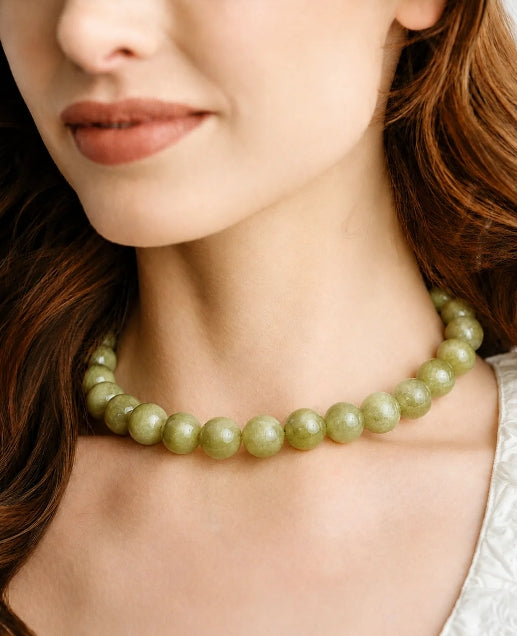 A close-up of a woman wearing a light green beaded necklace, showing the beads and her neck against her skin.