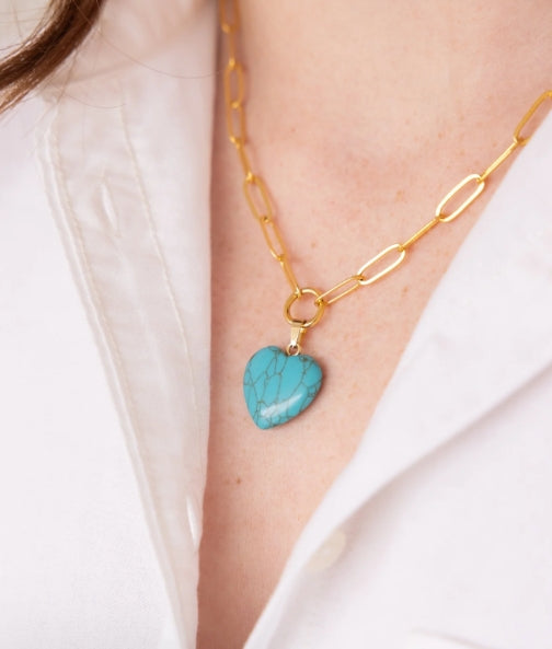 A gold chain necklace with a heart-shaped turquoise pendant, worn by a model in a white collared shirt.