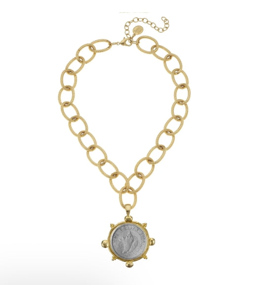 A gold chain necklace featuring a large circular pendant with a silver-toned coin in the center, displayed on a clean white background.