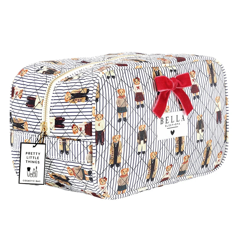 A quilted cosmetic pouch by Bella + Canvas featuring a navy and white pinstripe pattern with a repeating print of dogs in various outfits. The pouch has a gold zipper, a red bow, and a white brand tag.