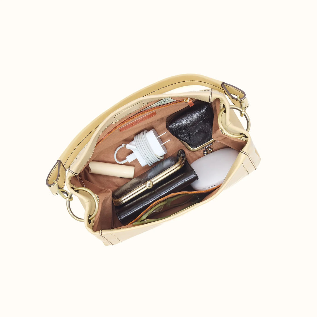 Open beige handbag with various items on a white background