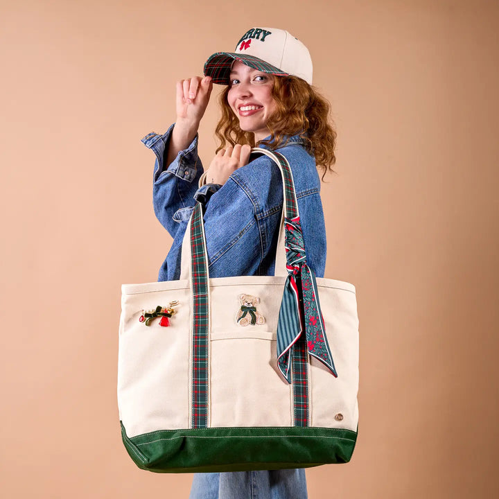 Person holding a beige tote bag with green accents and a colorful scarf, wearing a denim jacket and cap.