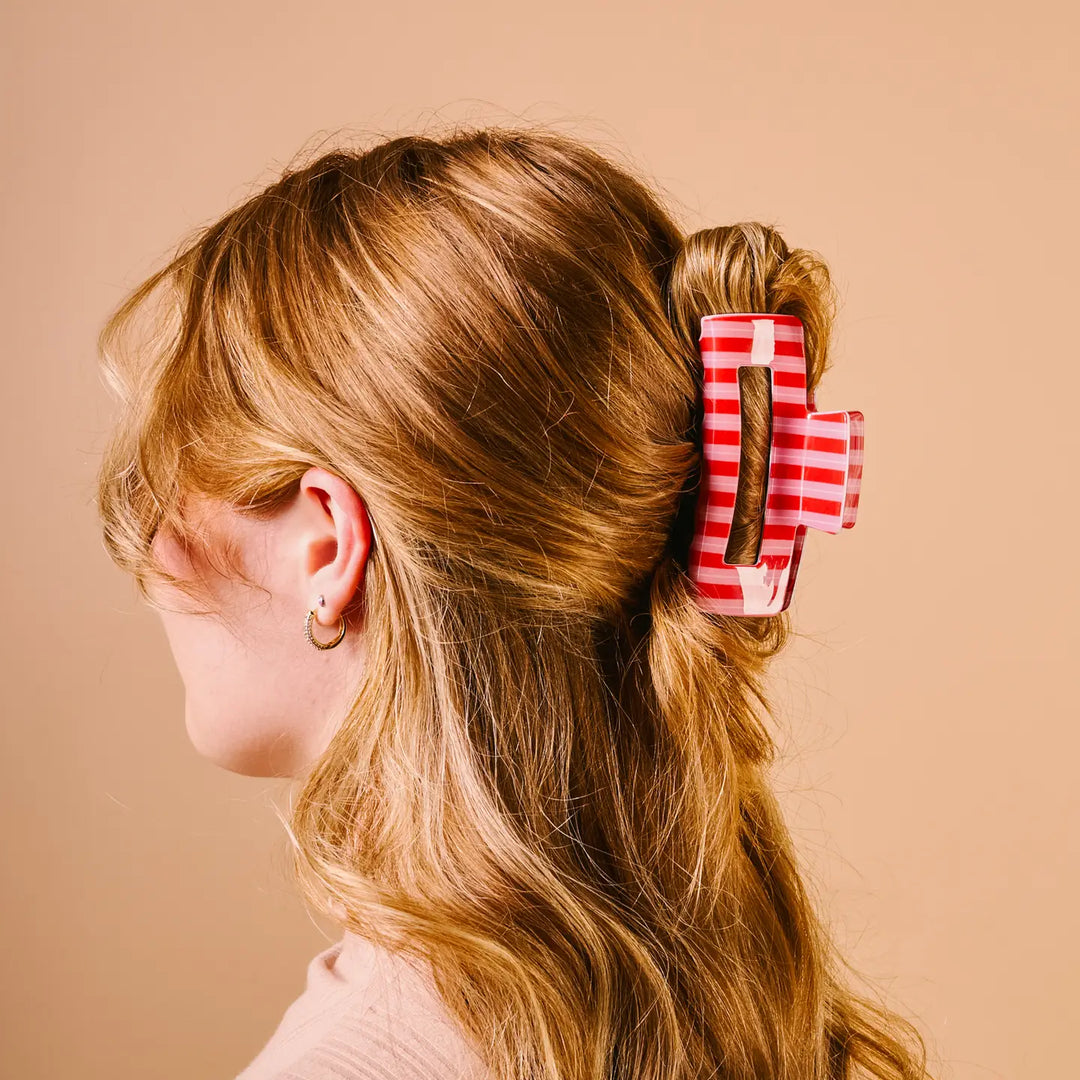 A side-profile view of a woman with light brown hair wearing a red and white striped claw clip in her hair, set against a solid beige background.