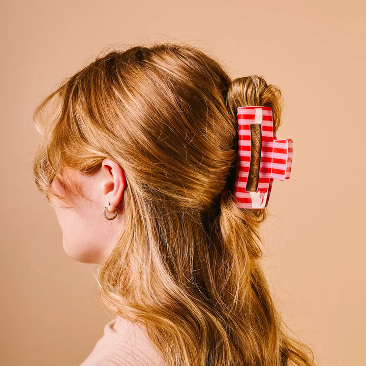 A side-profile view of a woman with light brown hair wearing a red and white striped claw clip in her hair, set against a solid beige background.